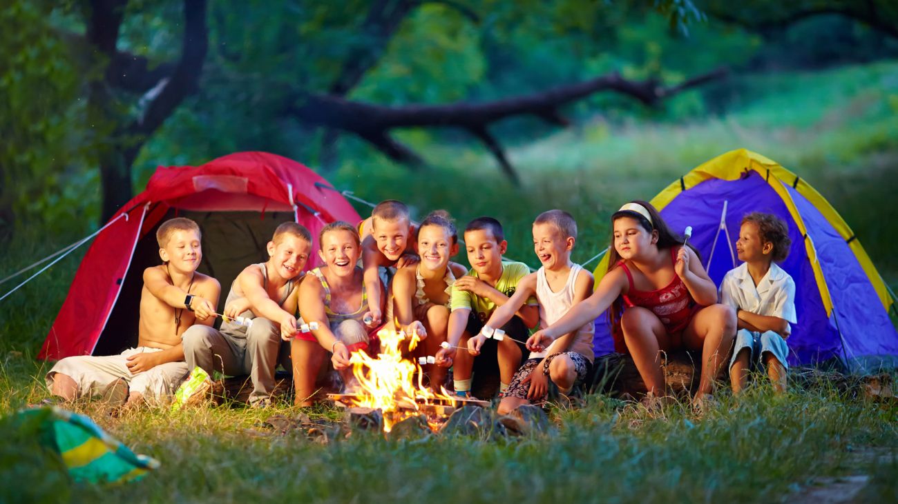 group of happy kids roasting marshmallows on campfire
